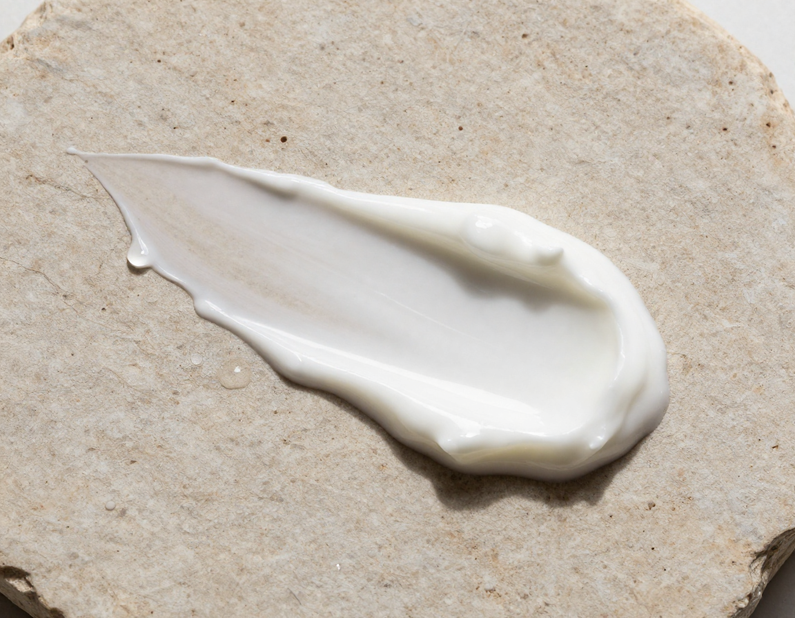 구멍이 뚫린 거친 돌 표면 위에 유분기가 도는 되직한 질감의 하얀 크림이 얹어져 있는 옆모습 사진입니다.