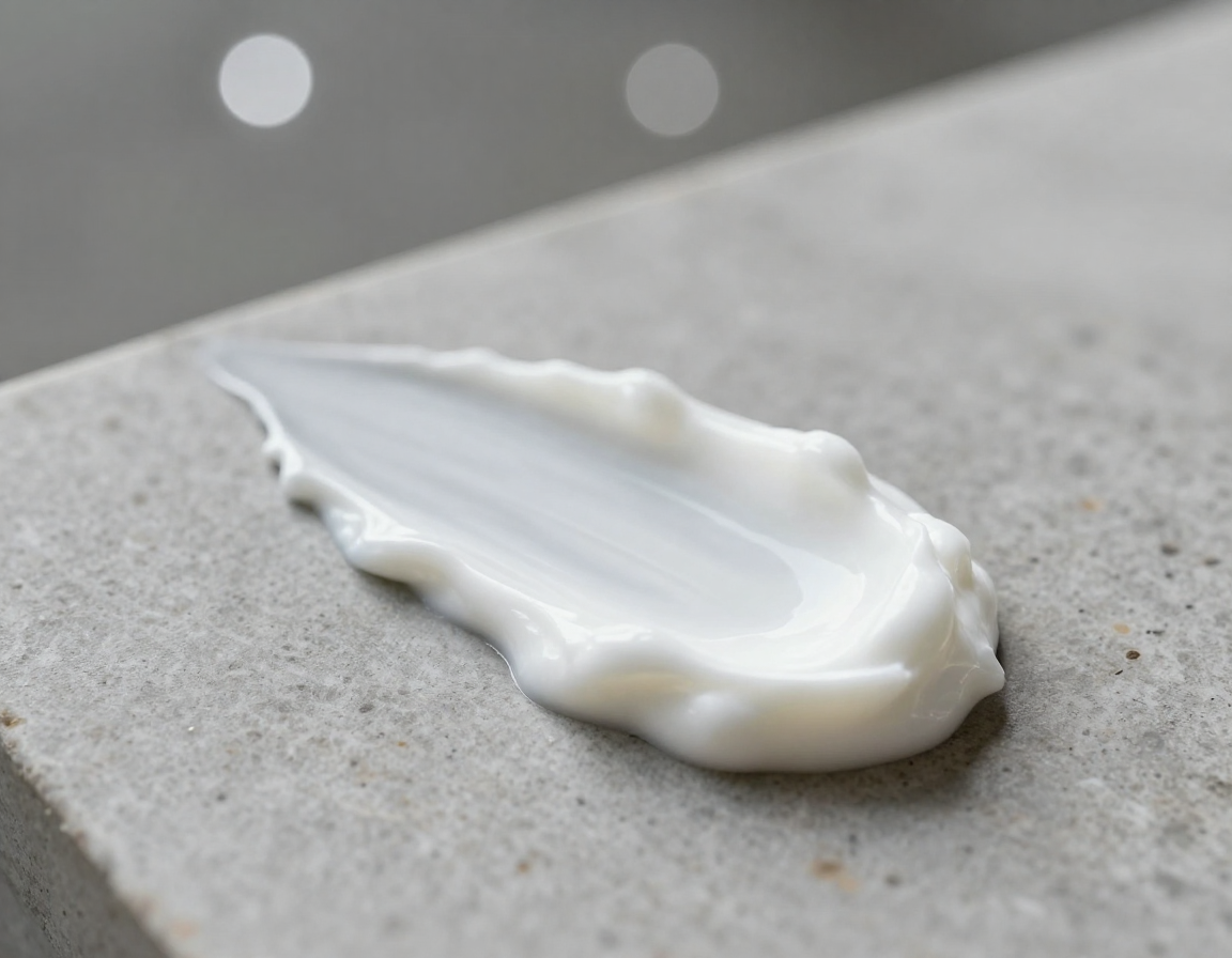 거친 돌 표면 위에 대각선 방향으로 부드럽고 두껍게 펴 발린 흰색 크림 제형과 보케 배경.