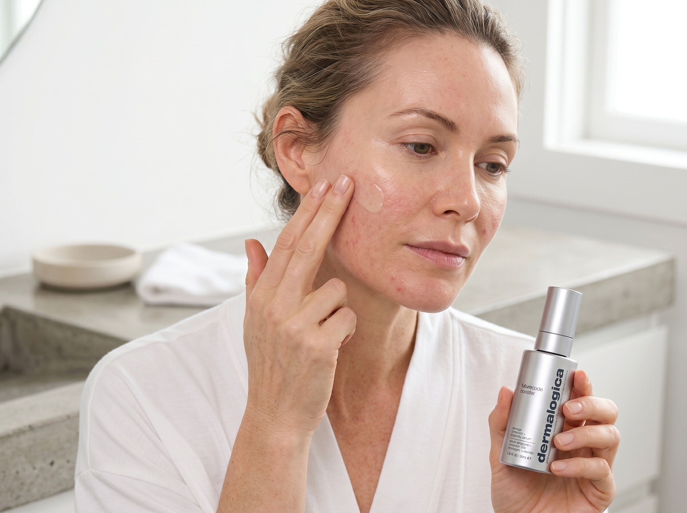 47-year-old Pacific Islander Australian woman with fair skin applying serum to her cheek in a bright bathroom, calm expression, morning light