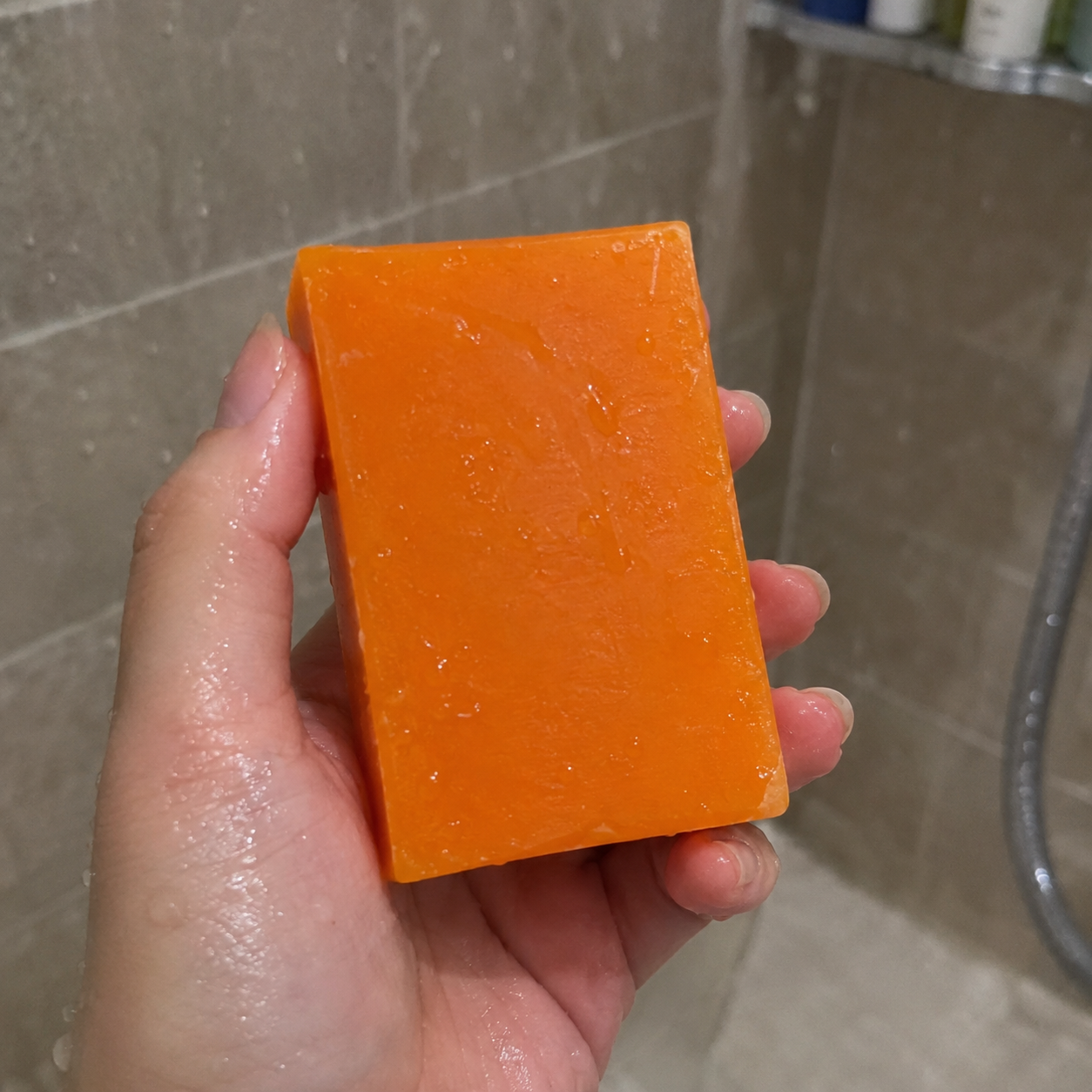 Hand holding VitaliQ persimmon soap bar in shower