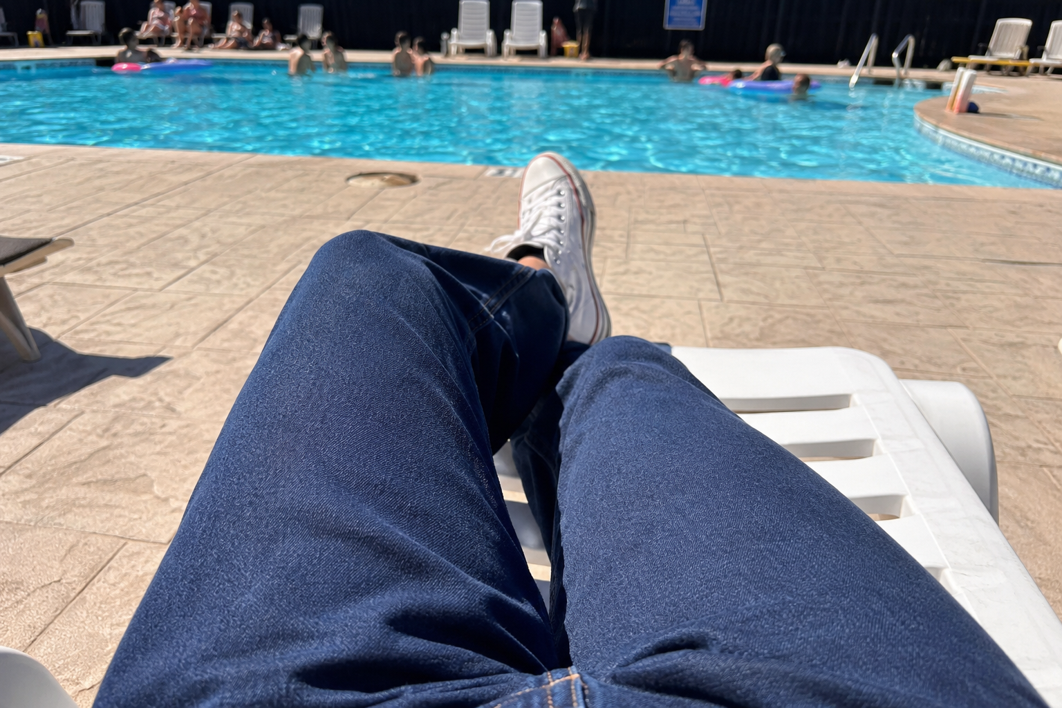 POV of my own legs in jeans and sneakers by the pool