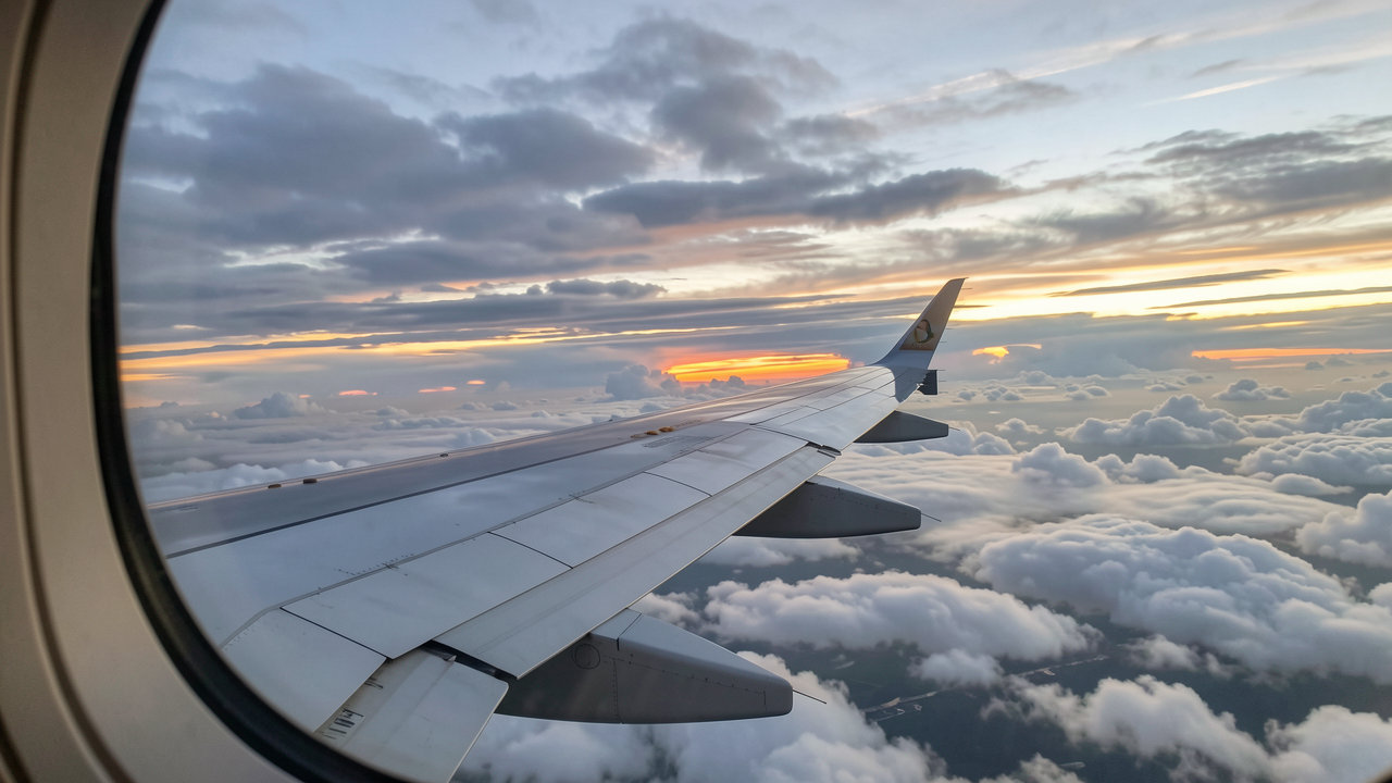 An airplane wing view from a cabin window against a cloudy sky during sunset, representing sustainable aviation fuel initiatives.