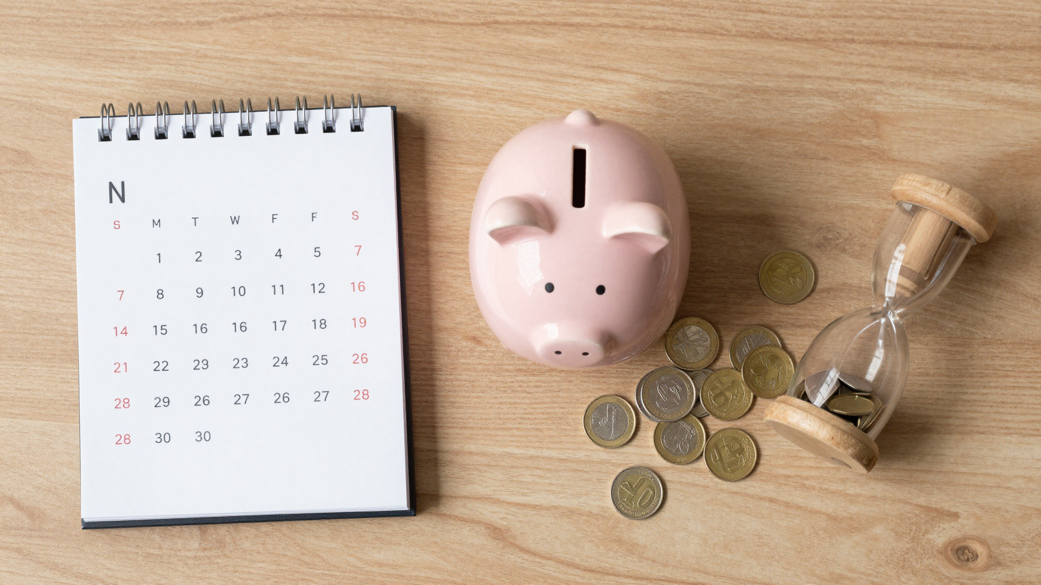 나무 책상 위 달력, 돼지저금통, 모래시계, 동전이 놓인 모습으로 국민연금 연기 수령의 혜택을 시각화한 이미지입니다.